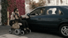 a woman in a wheelchair is sitting next to a blue car .