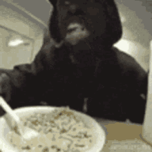 a man in a hoodie is eating a bowl of cereal