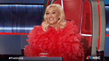 a woman in a red dress is sitting in a chair with a nbc logo on the bottom