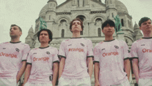 a group of men standing in front of a building wearing orange shirts