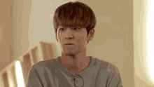 a young man with brown hair is making a funny face while wearing a gray shirt .