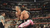 two wrestlers are fighting in a wrestling ring while a referee watches .