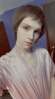 a young man wearing a choker necklace and a pink shirt takes a selfie