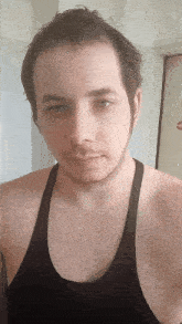 a man with a beard wearing a black tank top looks at the camera
