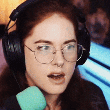 a woman wearing glasses and headphones talks into a green microphone