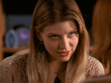 a woman wearing hoop earrings and a necklace looks at another woman
