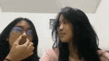 two girls are standing next to each other in a room and one is holding her nose .