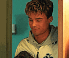 a young man with curly hair is holding a baseball glove and wearing a jacket with the letter s on it