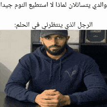 a man with a beard is sitting at a desk with his hands folded in front of him