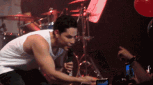 a man in a white tank top singing into a microphone in front of a crowd