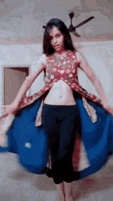 a woman is standing in a room wearing a blue skirt and a floral top .