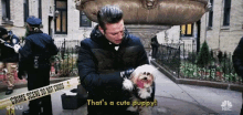 a man is holding a small white dog and saying that 's a cute puppy .