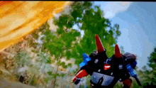 a robot with red horns is flying through the air with trees in the background