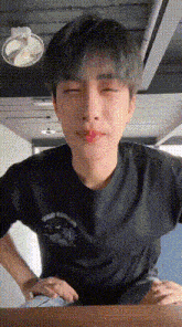 a young man wearing a black t-shirt is sitting at a table with his eyes closed .