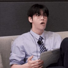 a man with glasses and a tie is sitting on a couch holding a tablet