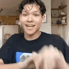 a young man in a black t-shirt is smiling while holding a video game controller .