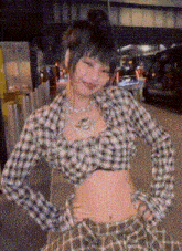 a woman wearing a plaid shirt and a plaid skirt is standing on a street with her hands on her hips .