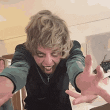 a man with a cross necklace is making a funny face with his hands outstretched .