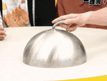 a person holding a metal dome on a table with chinese writing on the shirt