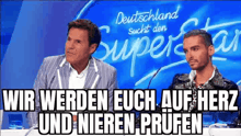 two men are sitting in front of microphones in front of a sign that says deutschland sucht den super star .
