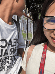a man wearing a white shirt that says oae on it stands next to a girl wearing glasses