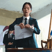 a woman in a suit and tie holds a piece of paper
