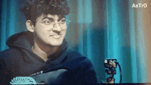 a man wearing glasses is sitting in front of a camera with astro written on the bottom of the screen