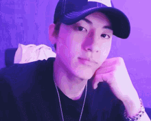 a man wearing a hat and a necklace is sitting in front of a purple background .