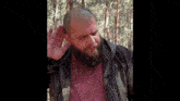 a man with a beard is holding his hand to his ear in a forest .