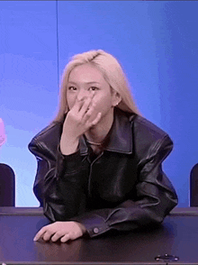 a woman in a leather jacket is sitting at a table with her hand on her face .