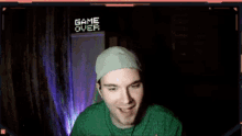 a man in a green shirt is screaming in front of a game over sign
