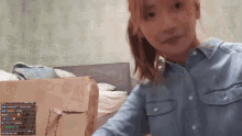 a woman in a denim shirt is standing next to a cardboard box .