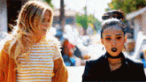 two women are standing next to each other on the street .