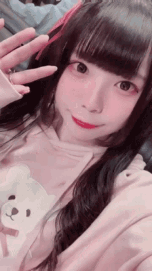 a girl wearing a pink hoodie with a teddy bear on it is taking a selfie