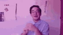 a man wearing glasses and a blue shirt is making a funny face while standing in front of a purple wall .