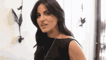 a woman in a black dress stands in front of a wall with feathers on it