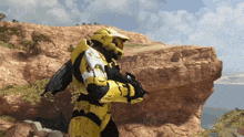 a man in a yellow armor is standing on top of a rocky hill near a body of water
