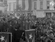 a black and white photo of a man giving a speech in front of a crowd of people
