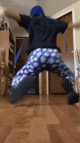 a person wearing blue pants and a black shirt is jumping in the air in a living room .