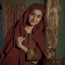 a woman in a red robe is standing next to a tree and smiling .
