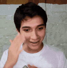 a young man wearing a white t-shirt is smiling and waving his hand