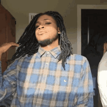 a man with dreadlocks and a beard wears a blue plaid shirt