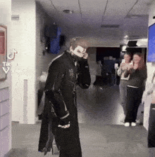 a man in a black coat is standing in a hallway with a mask on his face .
