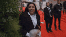 a woman in a suit is standing on a red carpet with other people