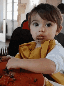 a little boy sitting at a table with a plate of food on it