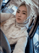 a woman wearing a hijab is taking a picture of herself in a car