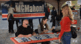 a man is signing autographs for a woman under a sign that says jim mcmahon