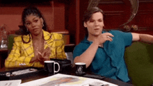 a man and a woman are sitting at a table with coffee cups .