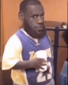 a man in a lakers jersey is standing in a room holding a cup of coffee .
