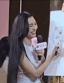 a woman with long black hair is holding a microphone and drawing a picture of a beaver on a white board .